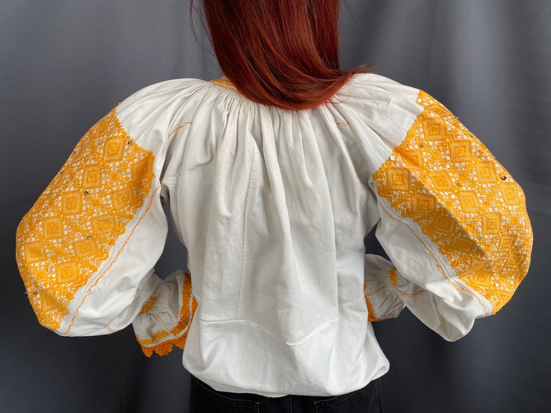 May include: White blouse with long sleeves and yellow embroidered details. The embroidery features a geometric pattern.