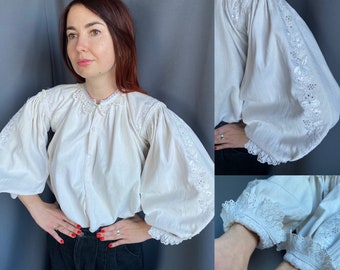 May include: A white blouse with a ruffled collar and long sleeves. The sleeves have delicate lace trim and embroidered details. The blouse is made of a lightweight fabric and has a relaxed fit.