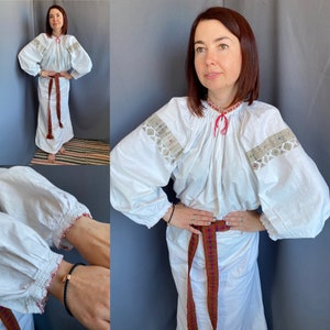 May include: White embroidered blouse with long sleeves and a gathered neckline. The blouse has a red and blue embroidered belt.