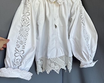 May include: White blouse with long sleeves, featuring intricate lace detailing on the sleeves and collar. The blouse has a button-down front and a scalloped lace hem. The sleeves are gathered at the cuffs.