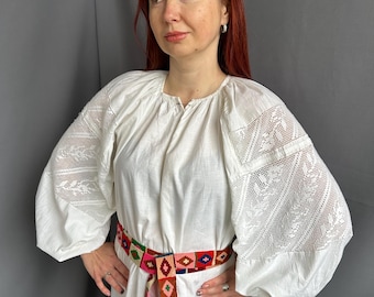 May include: A white linen dress with long sleeves and a colorful woven belt. The sleeves have intricate lace detailing.