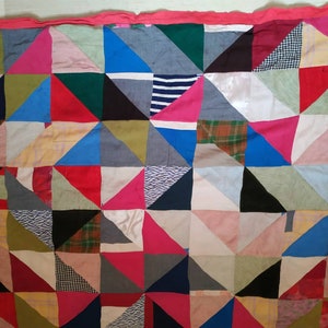 May include: A patchwork quilt made of various fabrics in different colors and patterns, including pink, blue, red, green, and black. The quilt is made of triangles sewn together to create a geometric design.