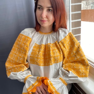 May include: A white embroidered blouse with yellow floral embroidery and crochet trim on the sleeves.