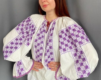 May include: White blouse with long sleeves and a purple embroidered design. The sleeves have a purple lace trim.