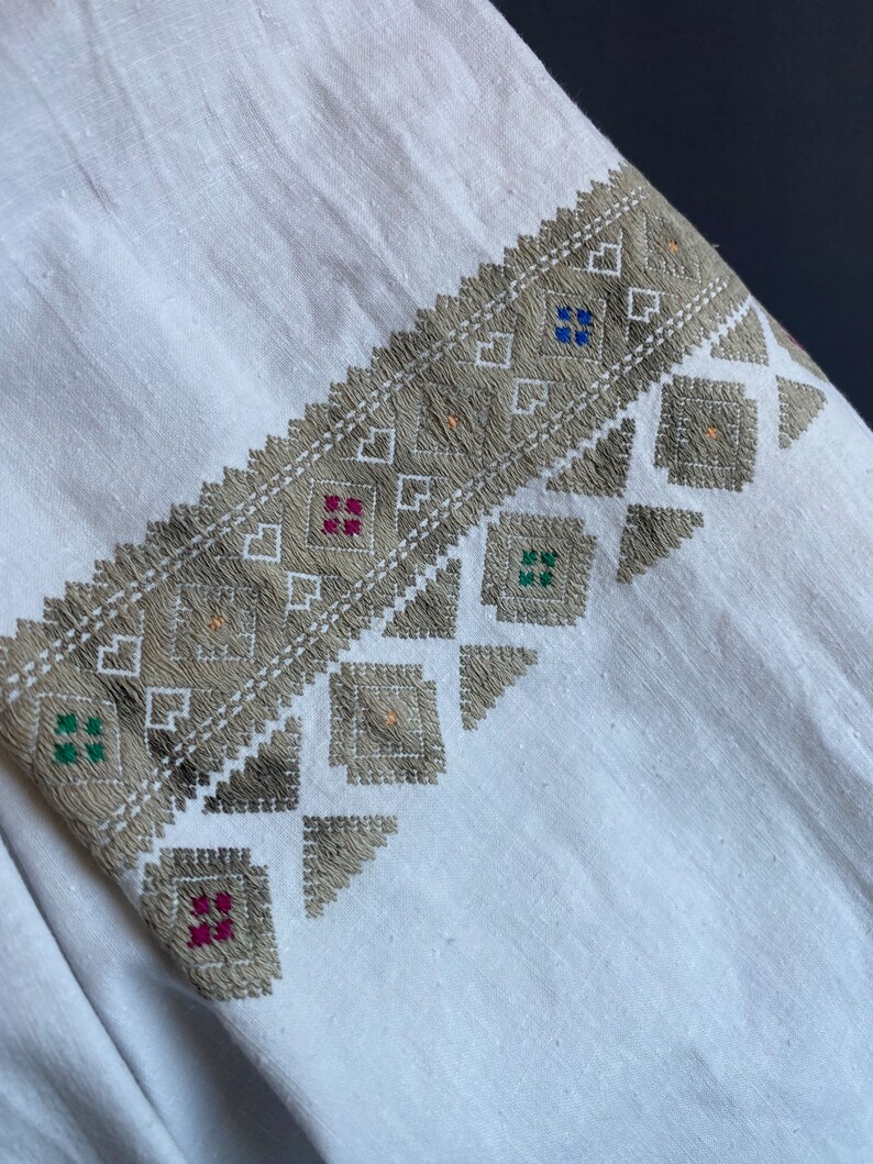 May include: White linen fabric with a gray embroidered design. The embroidery features geometric shapes and small squares in red, green, and blue.