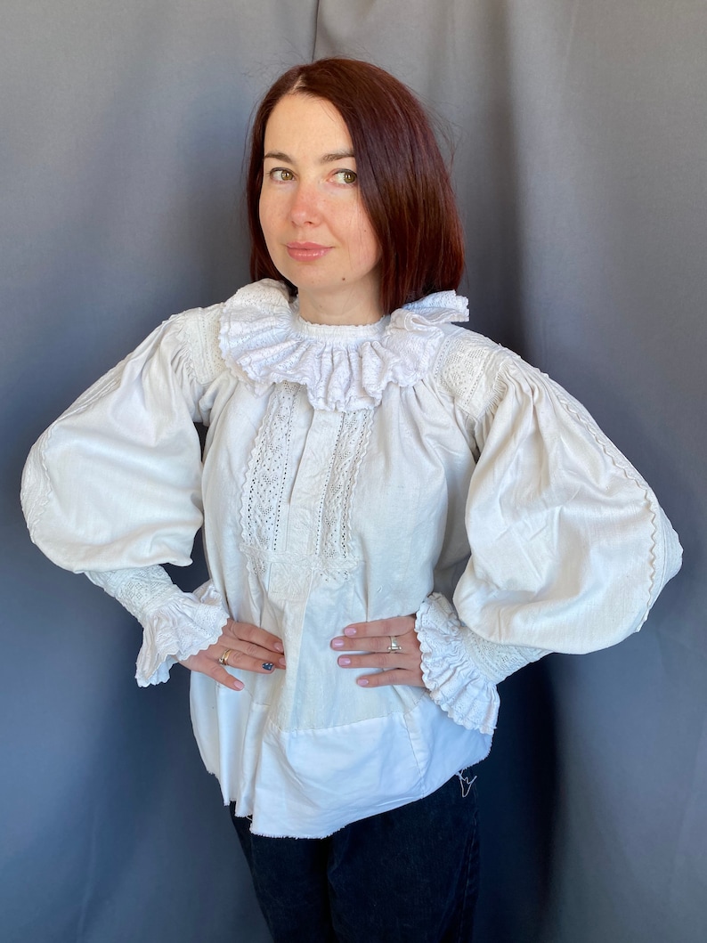 K&ouml;nnte beinhalten: Eine wei&szlig;e Bluse mit einem gro&szlig;en, gekr&auml;uselten Kragen und langen, bauschigen &Auml;rmeln. Die &Auml;rmel haben an den Manschetten Spitzenbesatz. Die Bluse ist aus einem leichten Stoff gefertigt und hat eine lockere Passform.
