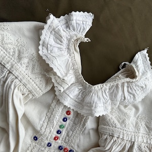 Op de afbeelding: Wit linnen blouse met een kanten kraag en kleurrijke geborduurde details.