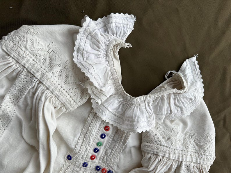 Op de afbeelding: Wit linnen blouse met een kanten kraag en kleurrijke geborduurde details.