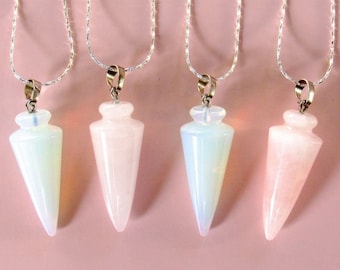 May include: Four gemstone pendulums on silver chains. The pendulums are in shades of white and pink, with a teardrop shape. The background is a solid light pink.
