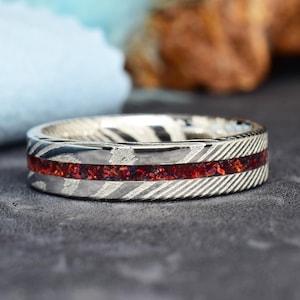 Può includere: Un anello d'argento con un'intarsio rosso. L'anello ha una superficie testurizzata e una fascia sottile.