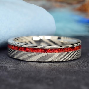 Può includere: Un anello d'argento con un'incisione di pietra rossa. L'anello ha un design a motivi ed è fatto di metallo.