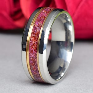 May include: A stainless steel ring with a gold band and a red and gold inlay. The ring is on a gray surface.