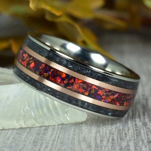 Peut inclure: Une bague en acier inoxydable avec un incrustation noire et deux bandes en cuivre. L'incrustation est remplie de morceaux d'opale rouge et orange.