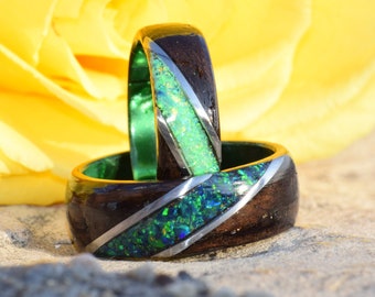 May include: Two wooden rings with a green and silver inlay. The rings are stacked on top of each other and are sitting on a light brown surface.