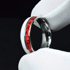 May include: A silver ring with a red and white inlay. The ring is made of stainless steel and has a polished finish.