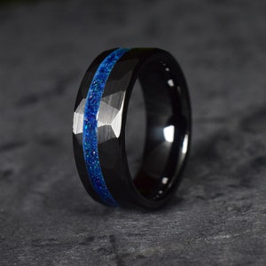 Puede incluir: Un anillo de carburo de tungsteno negro con una incrustaci&oacute;n azul. El anillo tiene un borde biselado y un acabado cepillado.