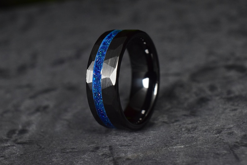 Puede incluir: Un anillo de carburo de tungsteno negro con una incrustaci&oacute;n azul. El anillo tiene un borde biselado y un acabado cepillado.