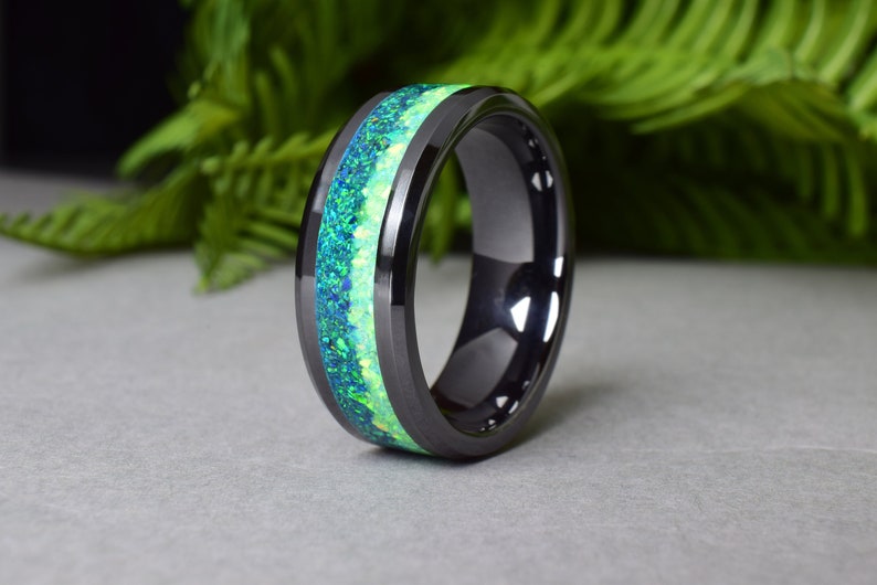 May include: A black ceramic ring with a green and white opal inlay. The ring is polished and has a beveled edge.