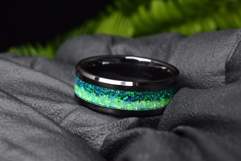 May include: A black tungsten carbide ring with a green and blue opal inlay.