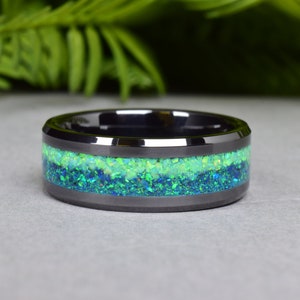 May include: A black ceramic ring with a green and blue opal inlay. The ring is a wide band with a beveled edge.