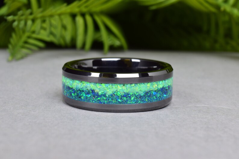 May include: A black ceramic ring with a green and blue opal inlay. The ring is a wide band with a beveled edge.