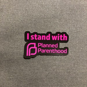 May include: A black and pink sticker with the text "I stand with Planned Parenthood".