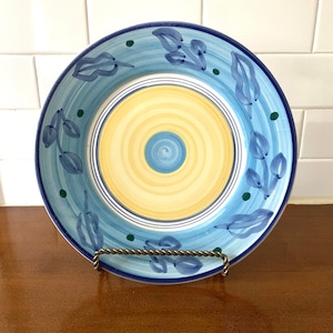 May include: A blue and yellow ceramic dinner plate with a swirl design in the centre and a leafy pattern around the edge.