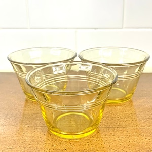 May include: Three yellow glass cups with a ribbed design. The cups are clear and have a slight yellow tint.