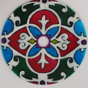 May include: A colorful stained glass design on a CD. The design features a central square with a white circle in the middle, surrounded by four red, blue, and green sections. The sections are decorated with white swirls and lines.