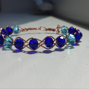 Peut inclure: Un bracelet en fil de cuivre avec des perles de verre bleues et turquoise. Les perles sont tissées en un motif en croisillon.