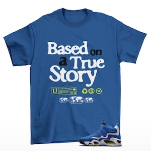 以下が含まれることがあります： 「Based on a True Story」の白文字がプリントされたロイヤルブルーのTシャツ。追加のグラフィックと、黄色のアクセントが付いた青と白のスニーカーが特徴です。