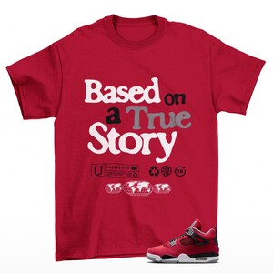 May include: A red t-shirt with the text "Based on a True Story" in white, black, and gray. The shirt features additional graphics and a pair of red and black sneakers.