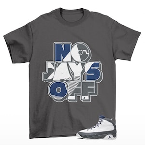 May include: A dark gray t-shirt with the text "NO DAYS OFF" in blue, white, and gray. A white and gray high-top sneaker with blue accents is positioned below the shirt.