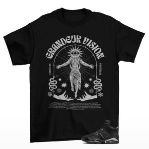 May include: Black t-shirt with a graphic design featuring the text "GRANDEUR VISION" and a figure with an eye in the center. The design includes snakes and stars. A pair of black and gray sneakers are at the bottom.