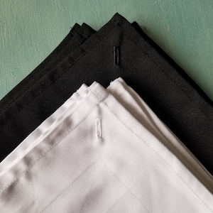 May include: Two black fabric napkins and one white fabric napkin, all folded in a triangle shape. Each napkin has a small button sewn in the center.