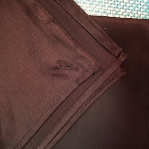 May include: Close-up of a dark brown fabric napkin folded in a triangle shape. The napkin has a single button sewn on the fold.