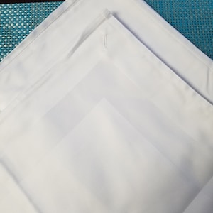 May include: Three white linen napkins folded in a triangular shape, with the top napkin folded over the other two.