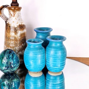 May include: Three blue ceramic vases with a striped pattern, sitting on a mirrored surface next to a brown and white ceramic pitcher and a green and blue marble.