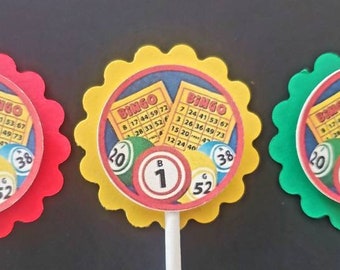 May include: Three colorful cupcake toppers with scalloped edges. Each topper features a bingo card with numbers and a bingo ball with the number 1. The toppers are red, yellow, and green.