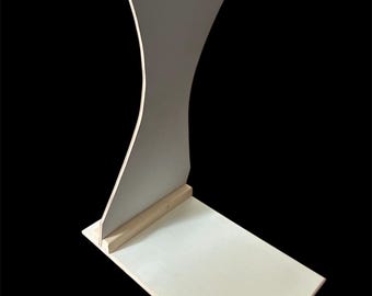 May include: A light-colored wooden display stand with a curved back and a rectangular base. The stand is made of unfinished wood and has a simple, modern design. The stand is suitable for displaying items.