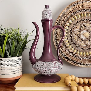May include: A purple ceramic teapot with a white crackle glaze and a decorative design. The teapot has a spout and a handle and sits on a wooden surface.