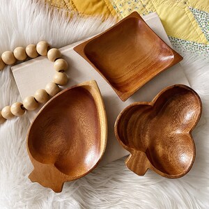 May include: Three wooden serving bowls in different shapes. The bowls are made of dark brown wood and have a natural, rustic finish. The bowls are perfect for serving snacks, dips, or salads.