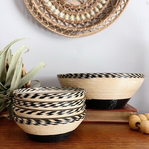 May include: A set of woven bowls with black and white stripes. The bowls are made of natural materials and have a rustic look. The bowls are stacked on top of each other and are sitting on a wooden surface.