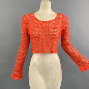 May include: A bright orange crochet top with long sleeves and a cropped fit. The top has a loose, open weave.