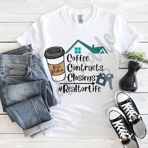 May include: White t-shirt with a teal house graphic and the text "Coffee Contracts Closings #RealtorLife". A coffee cup with the text "Best Realtor" is to the left of the house graphic. The t-shirt is on a wooden surface with a pair of blue jeans and black sneakers.