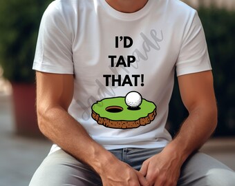 Pode incluir: Camiseta branca com o texto "I'D TAP THAT!" acima de um gráfico de uma bola de golfe em um green. A bola está perto de um buraco. A camiseta é de manga curta.