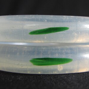 May include: Two white jade bangles with green jade accents. The bangles are smooth and polished.