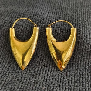 May include: A pair of gold hoop earrings with a pointed, triangular design. The earrings are made of a shiny metal and have a simple, elegant style.