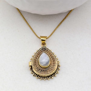 May include: A gold teardrop-shaped locket necklace with a white moonstone pendant. The locket has a detailed design with small gold beads around the edge.