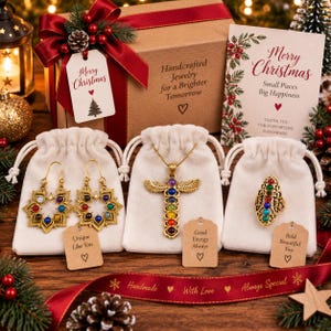 May include: A jewelry set featuring gold-toned earrings, a winged pendant necklace, and a ring, each adorned with multi-colored stones. The items are displayed with three white drawstring pouches, each with a small tag, inside a gift box with a red ribbon.